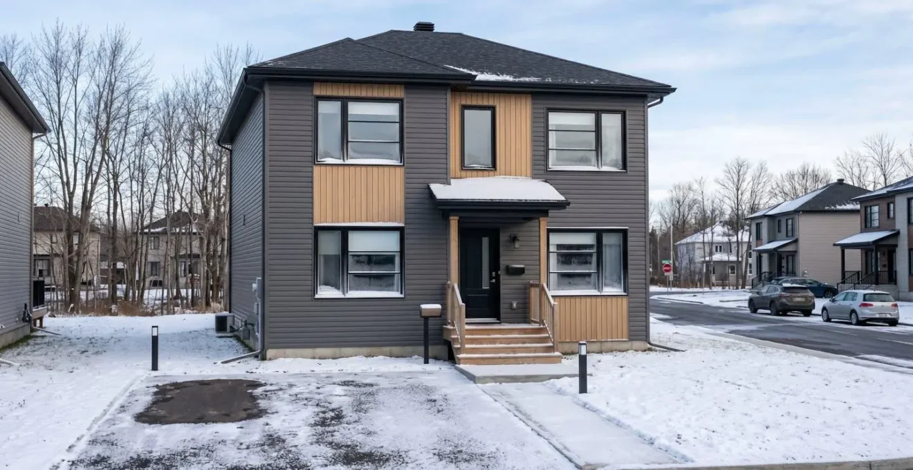 Façade d'une maison résidentielle québécoise moderne avec légère accumulation de neige sur les rebords de fenêtres et traces de gel visibles aux coins des cadres sous une lumière hivernale froide